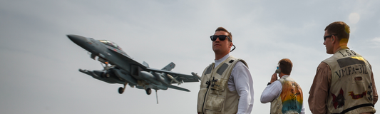 Crew members intently watch as a fighter jet approaches the deck. The image captures the anticipation of a potential 'bolter' scenario on an aircraft carrier, emphasizing the intricate choreography of naval aviation operations.