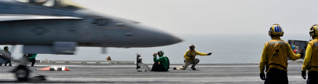 Close-up image of an aircraft carrier deck, highlighting a jet in motion and the essential roles of the crew. The scene depicts the precision and teamwork required for successful aircraft carrier operations.